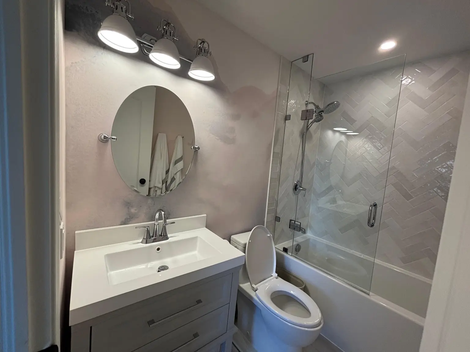 Finished bathroom renovation with herringbone wall tile, glass bath screen and updated vanity